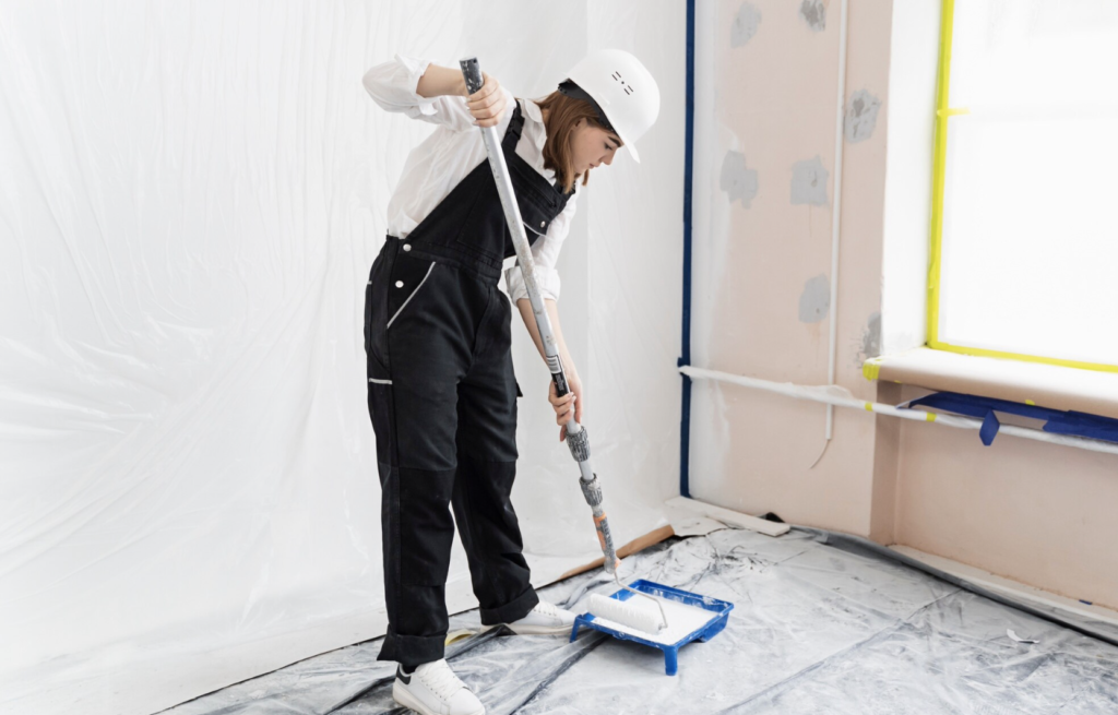 female house painter focusing on painting the interior of a house. Rolling the wall with hard hat and overalls. Loading the roller. 