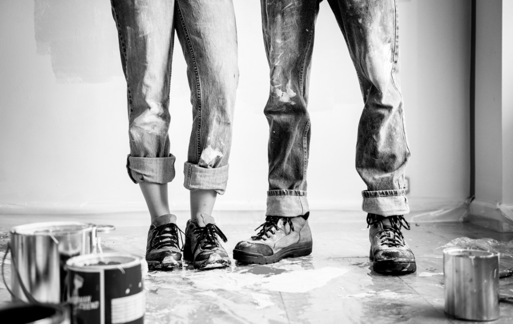 Two painters black and white standing in home with paint cans on the floor 